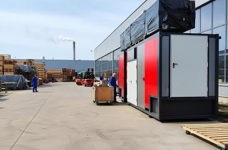 Kompletna kotłownia kontenerowa Plomex-Pol na placu przemysłowym. Widok na szaro-czerwony moduł mobilnej kotłowni z infrastrukturą logistyczną w tle, gotowy do instalacji u klienta.